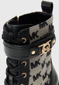 Stivale in pelle nera con lacci, con sovrapposizione in tessuto grigio a fantasia che presenta un logo. Accentuato con dettagli in oro e un anello per il tiro.