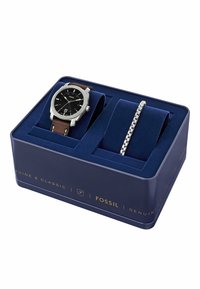 Reloj Fossil con esfera negra, caja plateada y correa de cuero marrón, acompañado de una pulsera de metal plateado, presentado en una caja azul con terciopelo.