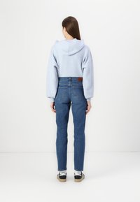 Lys blå oversized hettegenser med hette, kombinert med høytlivs blå denim jeans. Sko med sort og hvitt design fullfører antrekket.