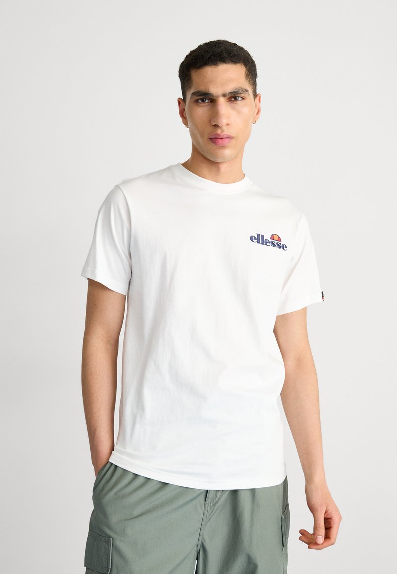 T-shirt bianca in cotone con un piccolo logo "ellesse" blu e arancione sul petto. Maniche corte, colletto girocollo, vestibilità rilassata e senza fantasie.