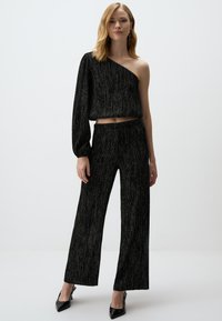 Top court noir à une épaule avec une manche longue et un pantalon large assorti, présentant une finition métallique texturée et une coupe décontractée.