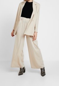 Béžový blazer, černý pletený top a široké béžové kalhoty, doplněné botami na blokovém podpatku s hadím vzorem. Hladká látka a uvolněný střih.