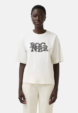 Bílý oversized tričko vyrobené z měkké tkaniny má výrazné černé grafické logo s jemnými detaily. Krátké rukávy a uvolněný střih.
