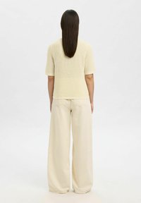 T-shirt en tricot à manches courtes de couleur jaune clair avec un motif en nid d'abeille texturé, associé à un pantalon large beige clair. Deux poches arrière visibles.