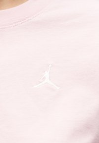 Λευκό κεντημένο περίγραμμα ενός παίκτη μπάσκετ που πηδάει με την μπάλα σε ανοιχτό ροζ ύφασμα, κοντά στον στρογγυλό λαιμό ενός ρούχου.