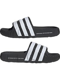 Crne natikače s reljefnim remenom na kojem se nalaze tri bijele pruge. Potplat je izbrušen za bolje prianjanje, a brend je otisnut sa strane.