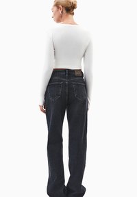 Biała, długa bluzka typu crop top z długim rękawem, zestawiona z ciemnoniebieskimi dżinsami z wysokim stanem, charakteryzującymi się luźnym krojem i widocznymi kieszeniami z tyłu.