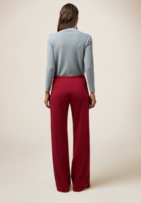 Lichtgrijze gebreide trui met lange mouwen, gecombineerd met hoge taille, wijdvallende rode broek. Smooth textuur, minimale accenten.