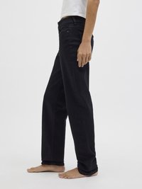 Μαύρα τζιν με ίσια γραμμή, σχέδιο πέντε τσεπών και εμφανείς ραφές, συνδυασμένα με ένα λευκό μπλουζάκι.