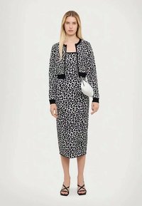 Melnā un baltā leoparda rakstā tērps ar pieguļošu siluetu, garām piedurknēm un īsu kardigānu. Iezīmējas ar melnu apdari un melniem sandaliem ar siksniņām.