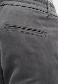 Pantaloni di tessuto grigio con una consistenza liscia, vita piegata e una piccola tasca a filetto sul retro, cucita con cura.