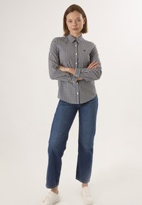Camicia a quadri bianco e nero con maniche lunghe, chiusura con bottoni e colletto. Indossata con jeans blu e sneakers bianche.