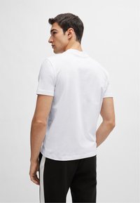 T-shirt bianco a maniche corte in cotone, con collo rotondo e una trama liscia, indossato con pantaloni neri con una striscia laterale bianca.