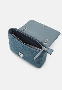 Vadderad blå tyghandväska med dragkedjestängning, silverfärgad hårdvara och en slät, kontrasterande klaff. Inuti finns flera fack.