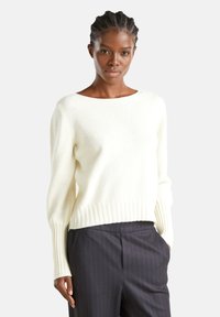 Maglione a maglia color crema con scollatura rotonda, polsini a coste e orlo inferiore, abbinato a pantaloni scuri a righe.