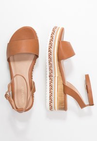Sandales à plateforme en cuir marron avec de larges brides, boucle à la cheville ajustable et semelle texturée multicouche avec des accents crème et marron.