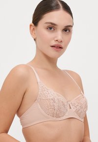 Bralette s čipkastim rubom u mekoj boji kože, s delikatnim cvjetnim uzorkom, podesivim trakama i glatkom teksturom za udobnost.