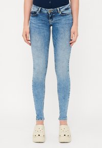 Svijetloplavi traper skinny traperice s izbljeđenim završetkom, pet džepova i zatvaranjem na gumb. Uparene s bijelim klompi na slip-on.