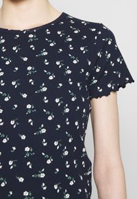 Top floreale navy in tessuto a coste, con piccoli fiori bianchi e steli verdi, scollatura rotonda e maniche corte scallop.