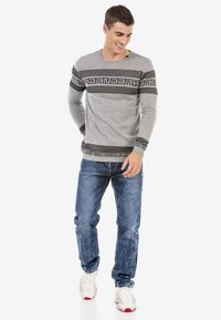 Graues Langarmshirt mit schwarzen horizontalen Streifen und Textmuster, kombiniert mit hellblauen, zerrissenen Jeans und weißen Sneakers.