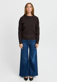 Mörkbrun tröja med strukturerat mönster, rund hals, och långa ärmar, tillsammans med vida blå jeans i denim och svarta spetsiga ballerinas.