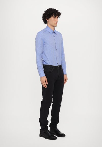 Hellblaues Button-up-Hemd mit dünnen weißen Streifen, kombiniert mit schwarzen Jeans und schwarzen Schuhen. Das Hemd hat einen Kragen und lange Ärmel.