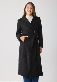 Black wool blend coat with a textured finish, wide lapels, a belt at the waist, and side pockets. Features a gold button detail.