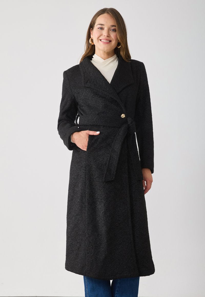 Black wool blend coat with a textured finish, wide lapels, a belt at the waist, and side pockets. Features a gold button detail.