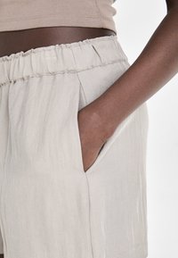 Light beige shorts with an elastic waistband, featuring side pockets and a smooth, slightly textured fabric.