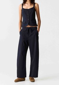 Ensemble deux pièces bleu marine à fines rayures, composé d'un gilet ajusté à boutons et d'un pantalon à jambes larges avec une taille élastique et des poches.