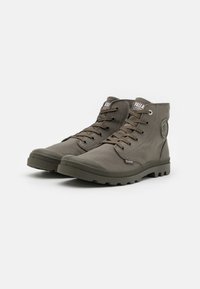 Botas de tobillo de lona color verde oliva con punta de goma, cordones resistentes y suelas texturizadas. Presenta un logo redondo en el lateral.