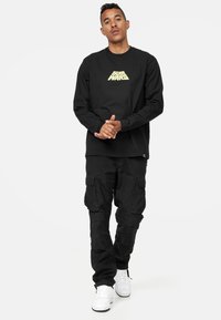 Svart långärmad t-shirt med en guldig "Star Wars" logotyp på bröstet, ihopparad med svarta cargobyxor och vita sneakers. Avslappnad passform och stil.