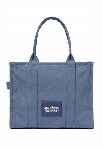 Bolsa de lona en azul, con dos asas resistentes, una forma rectangular espaciosa y una etiqueta con texto blanco que detalla la marca y el año.