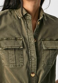 Olivgrön knapp-up skjorta i en bomullsblandning, med två bröstfickor, rundad krage och naturliga träknappar. Mjuk struktur.