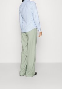 Helles blaues Hemd mit langen Ärmel, kombiniert mit locker sitzenden, hellgrünen Hosen. Strukturierter Stoff, simples Design, lässige Passform.