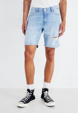 Shorts de mezclilla azul claro con un área desgastada, cortados por encima de la rodilla, combinados con zapatillas altas negras y calcetas blancas.