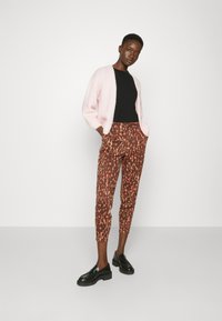 Pink, fluffy cardigan over a black top, paired with brown patterned pants featuring orange accents. Black loafers complete the look.
