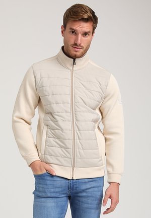Beige miksētās mediju jaka ar quilted priekšpusi, ribotām piedurknēm un augstu apkakli. Iekļautas rāvējslēdzēja aizdare un sānu kabatas.