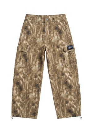 Loose-fitting brown and beige camouflage cargo pants with side pockets worn with white sneakers and a white shirt.