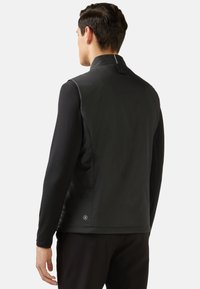 Veste sans manches noire avec un col haut, présentant une texture lisse, une fermeture éclair à l'avant et un accent de logo près de l'ourlet.
