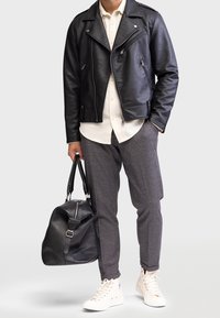 Zwart leren motorjack, wit shirt, grijs gemusterd broek, zwarte duffeltas en witte high-top sneakers.