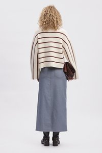 Pull crème avec des rayures marron, design court, associé à une longue jupe en denim bleu. Des bottines en cuir noir complètent le look.