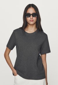 T-shirt in cotone grigio antracite, maniche corte, scollatura rotonda, vestibilità rilassata, texture liscia, abbinato a occhiali da sole neri a forma rettangolare.