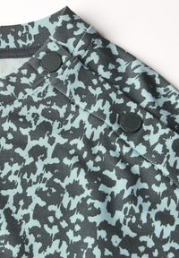 Tkanina s šedým a světle modrým vzorem, která má měkkou texturu, s černými knoflíky na rameni, což vytváří jedinečný design.