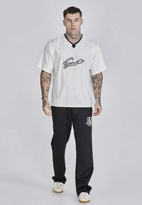 Maglia bianca a maniche corte con logo nero ricamato, abbinata a pantaloni da tuta neri con monogramma bianco, entrambi a vestibilità comoda.
