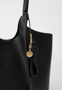 Schwarze Leder-Tote mit strukturierter Oberfläche, ausgestattet mit einem geflochtenen Lederakzent und einem goldenen Hardware-Tag, das durch eine Kette befestigt ist.