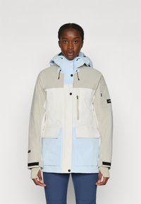 Värviblokkidega jope, mis sisaldab heledat beeži, valget ja helesinist paneeli. Valmistatud siledast ja kergest materjalist ning varustatud reguleeritava kapuutsi ja taskutega.