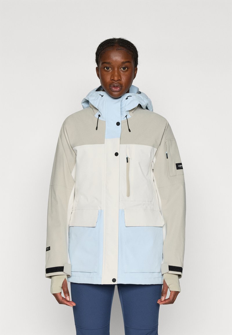 Värviblokkidega jope, mis sisaldab heledat beeži, valget ja helesinist paneeli. Valmistatud siledast ja kergest materjalist ning varustatud reguleeritava kapuutsi ja taskutega.