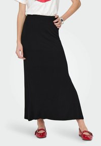 Zwarte maxi rok van zacht, rekbaar materiaal met een elastische tailleband, gecombineerd met rode schoenen met strikdetails en studs.