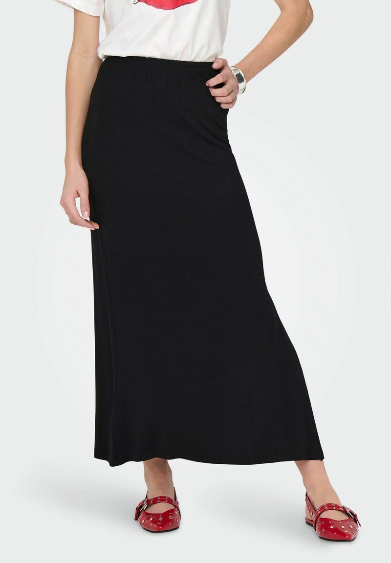 Zwarte maxi rok van zacht, rekbaar materiaal met een elastische tailleband, gecombineerd met rode schoenen met strikdetails en studs.